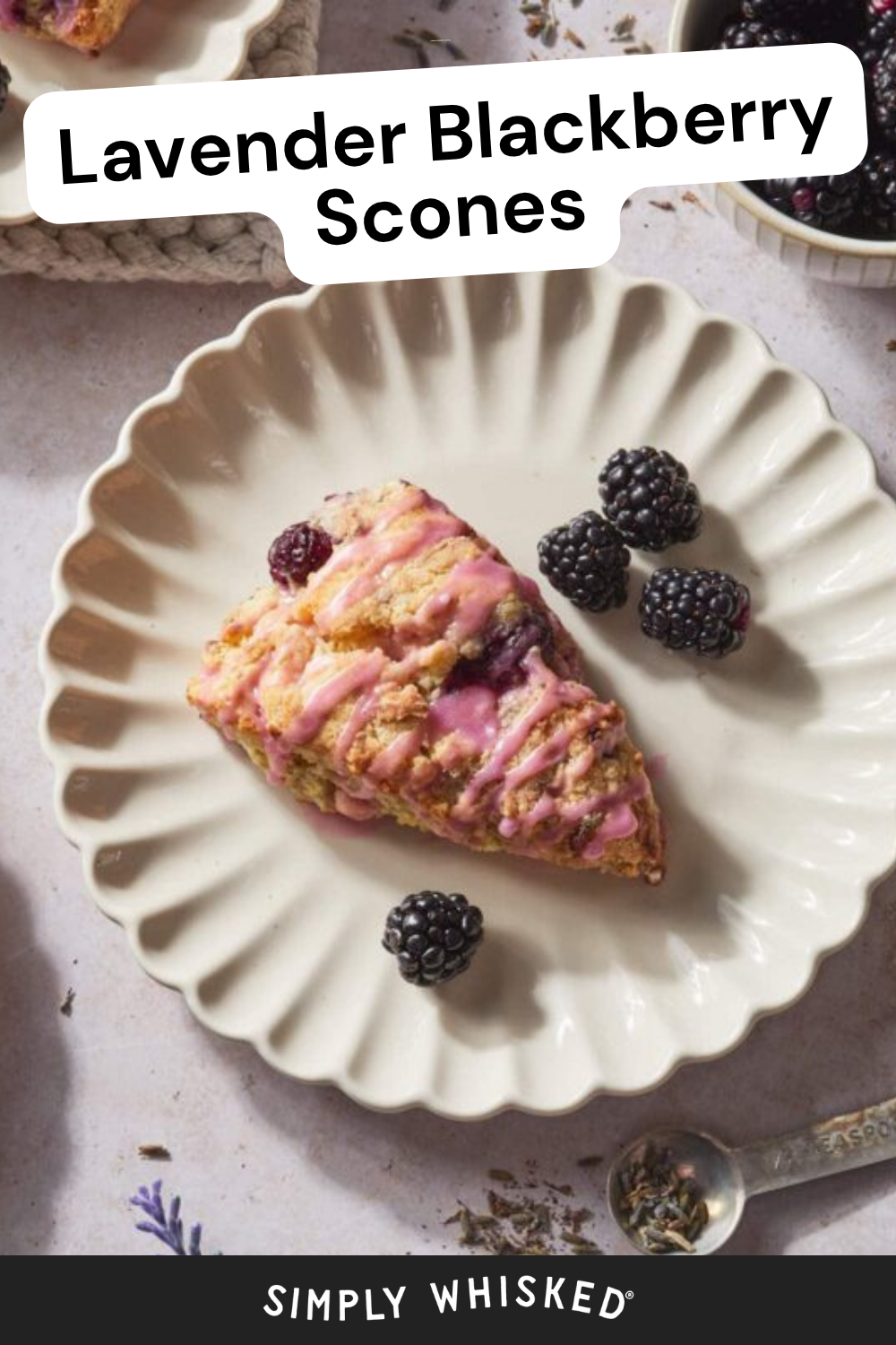 A lavender blackberry scone with pink glaze is on a scalloped cream plate, garnished with fresh blackberries. The text reads Blackberry Scones at the top and Simply Whisked at the bottom.