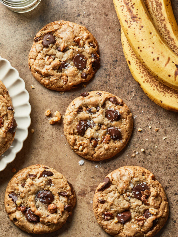 A few cookies spread out next to a plate of cookies and a few bananas.