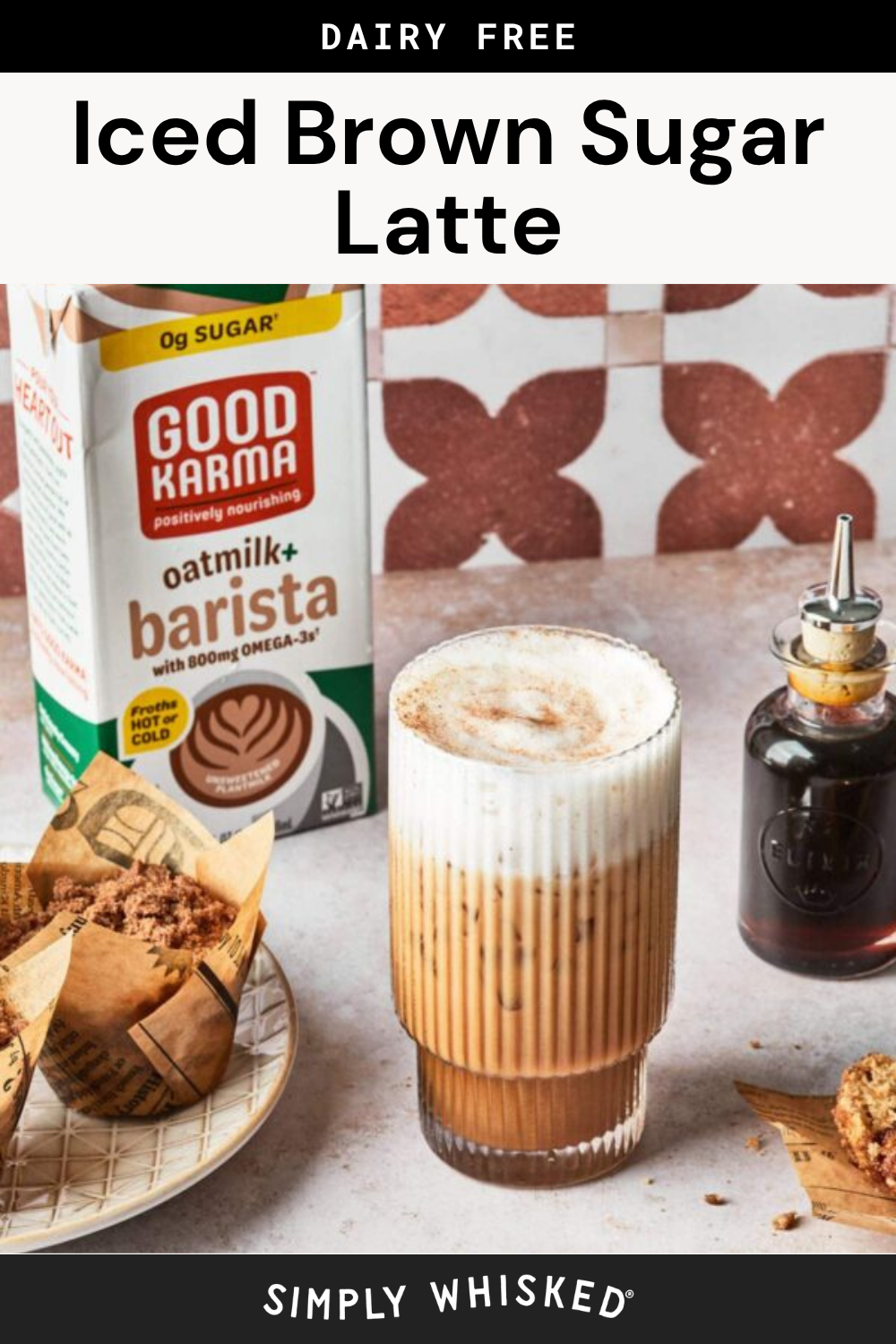 A glass of iced brown sugar latte with oatmilk sits on a table alongside muffins, a Good Karma oatmilk carton, and a bottle of syrup against patterned tiles. Text reads Dairy Free Iced Brown Sugar Latte.