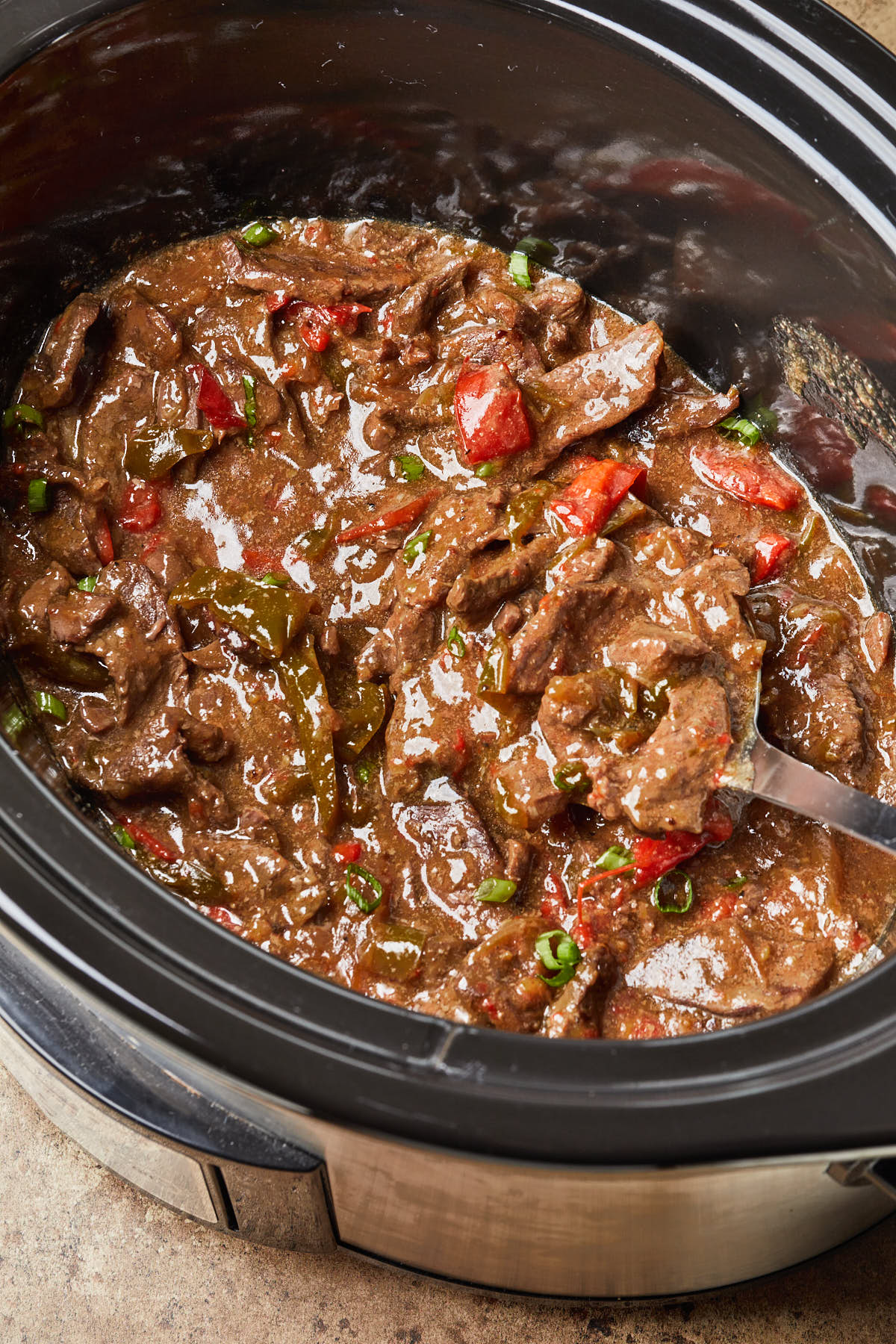Close up of pepper steak in sauce, in a slow cooker pot. 