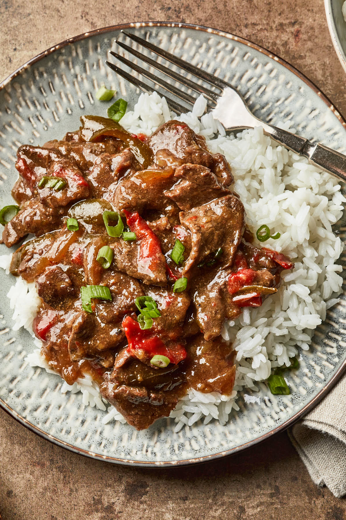 A close up of pepper steak on a plate, served over white rice. 