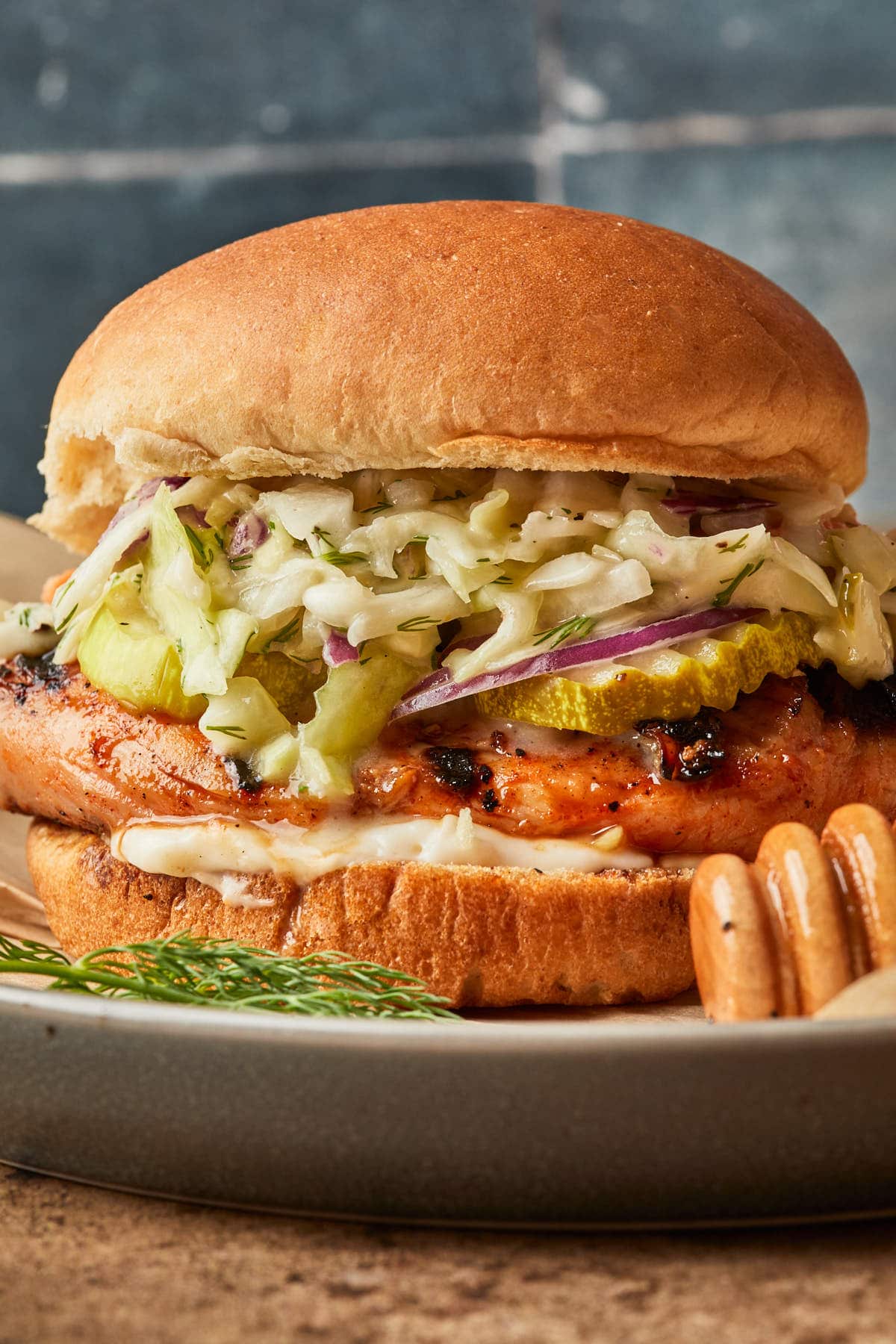 Close up of a chicken sandwich on a bun, topped with pickles, onions and pickle slaw with mayo. 