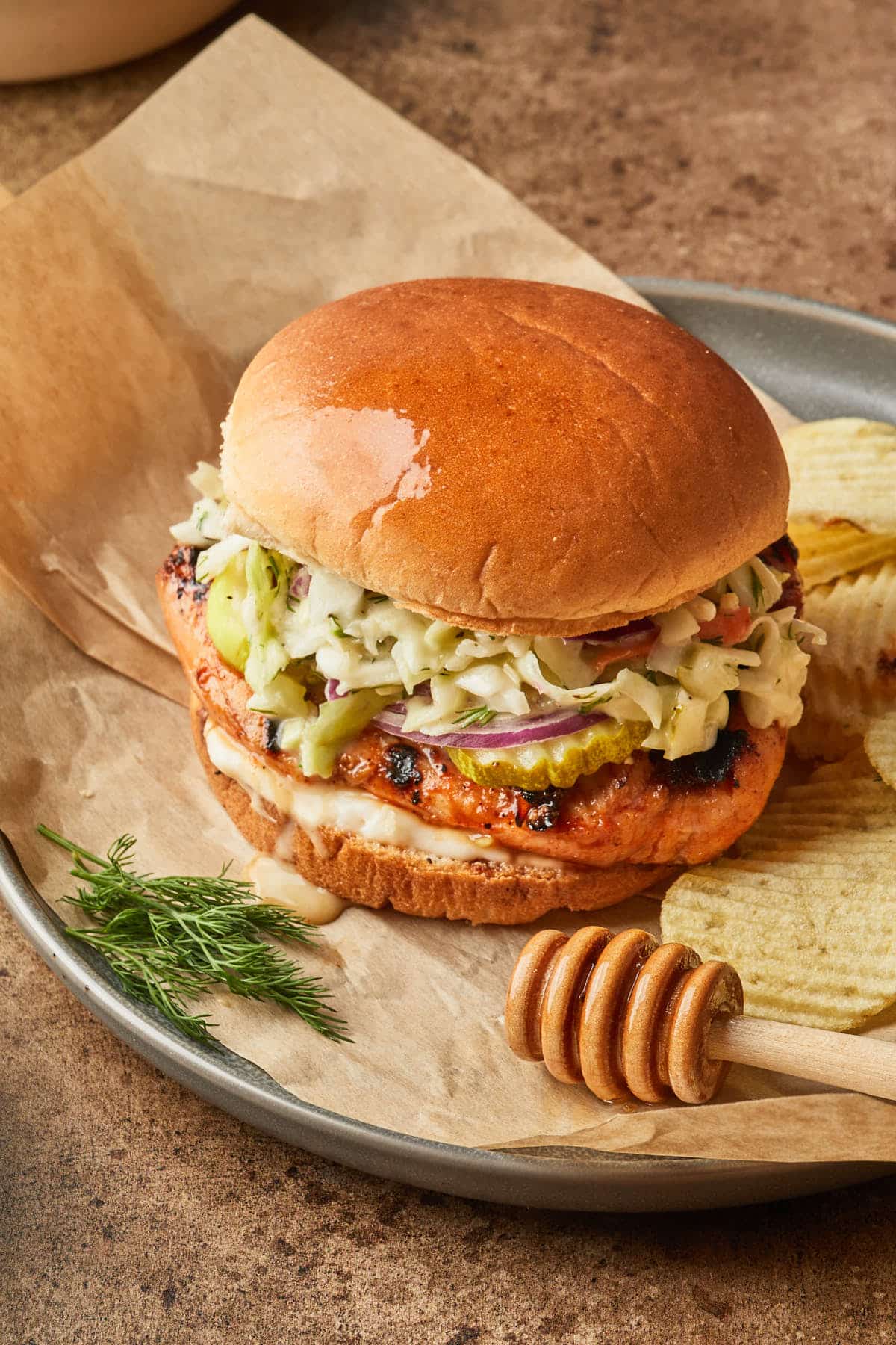 A grilled chicken sandwich on a serving platter with chips. 