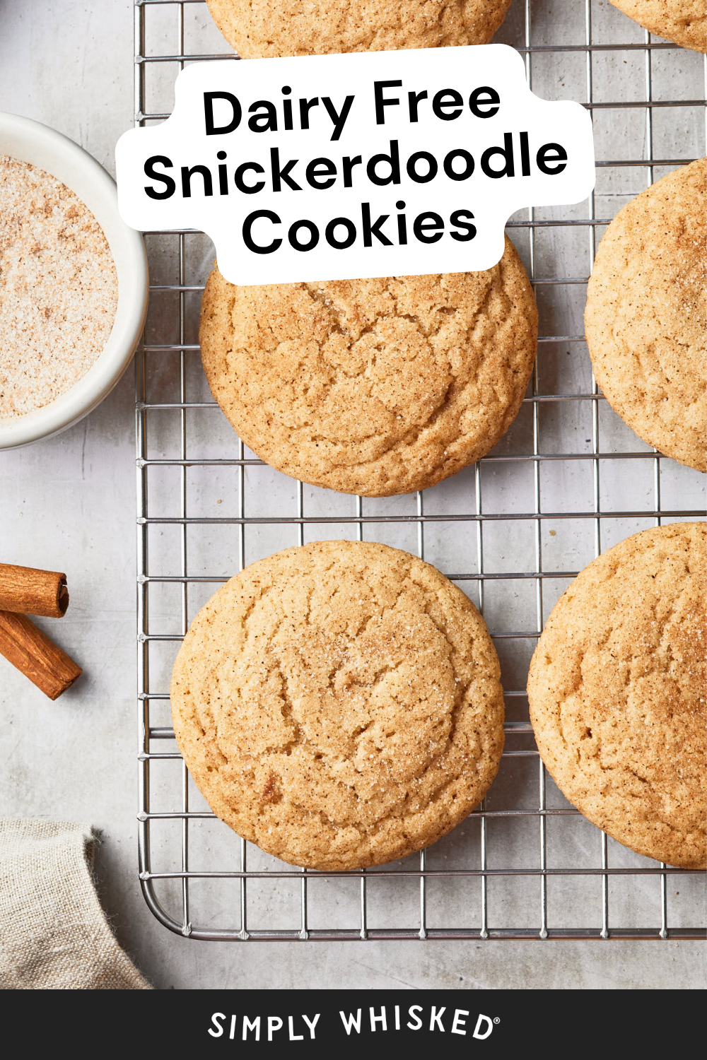 Five snickerdoodle cookies rest on a cooling rack with a bowl of cinnamon sugar and cinnamon sticks nearby, perfectly capturing the essence of classic snickerdoodle cookies. Text reads: Dairy Free Snickerdoodle Cookies. The bottom says SIMPLY WHISKED.