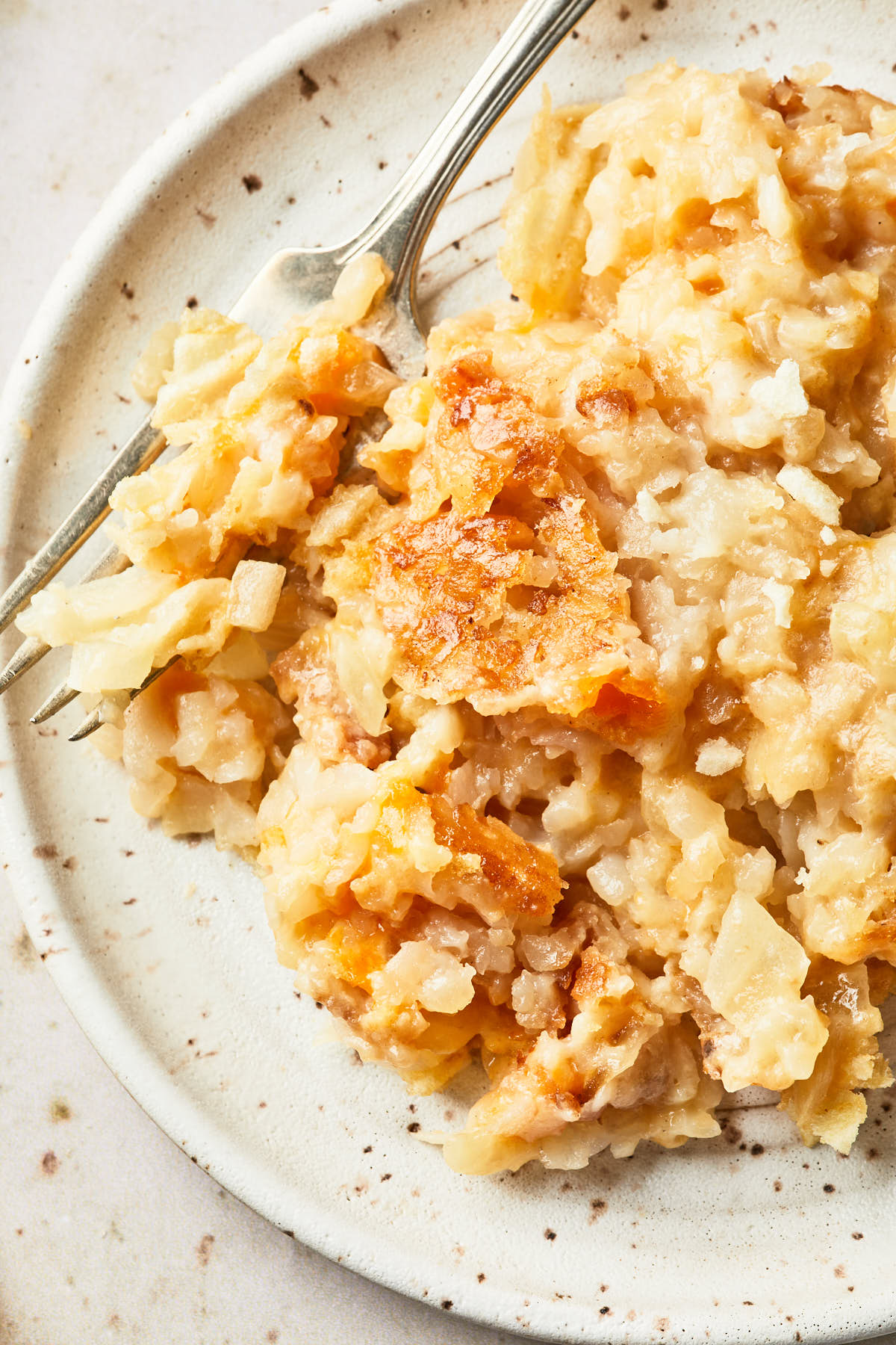 A close-up of a single serving of dairy-free cheesy potato casserole on a small speckled plate, showcasing the golden, crispy edges and creamy potato filling.