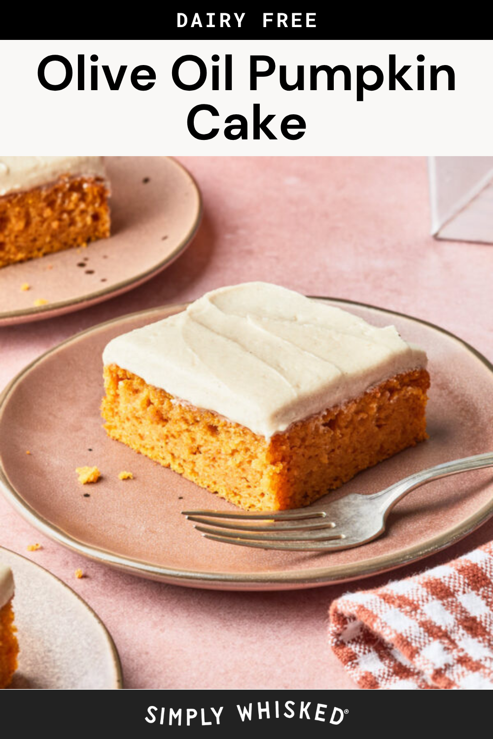 A slice of dairy-free Olive Oil Pumpkin Cake with frosting sits on a pink plate with a fork, next to a checkered napkin. Another plate with this moist, golden cake is in the background.