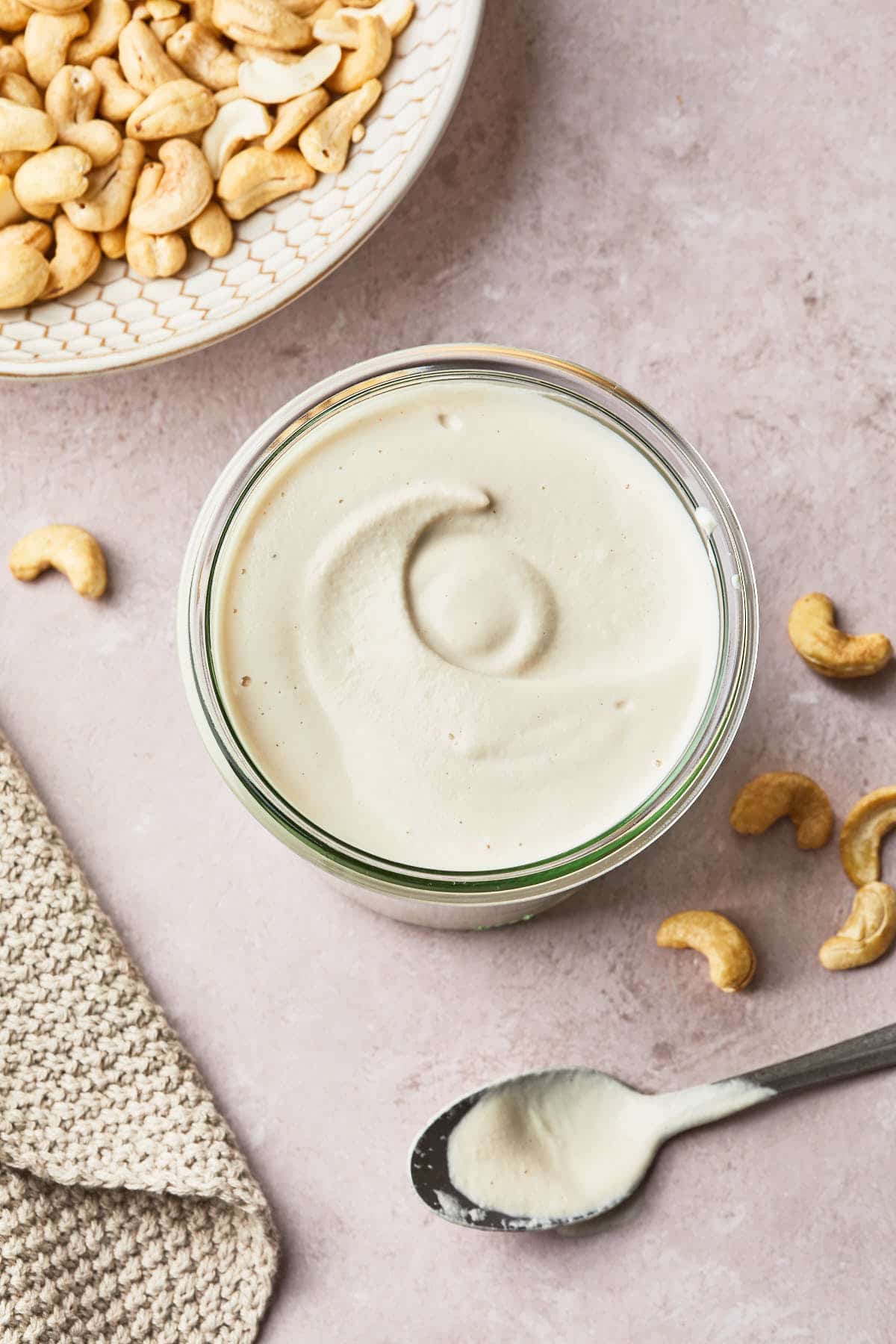 cashew cream in a large jar with a bowl of cashews and a spon
