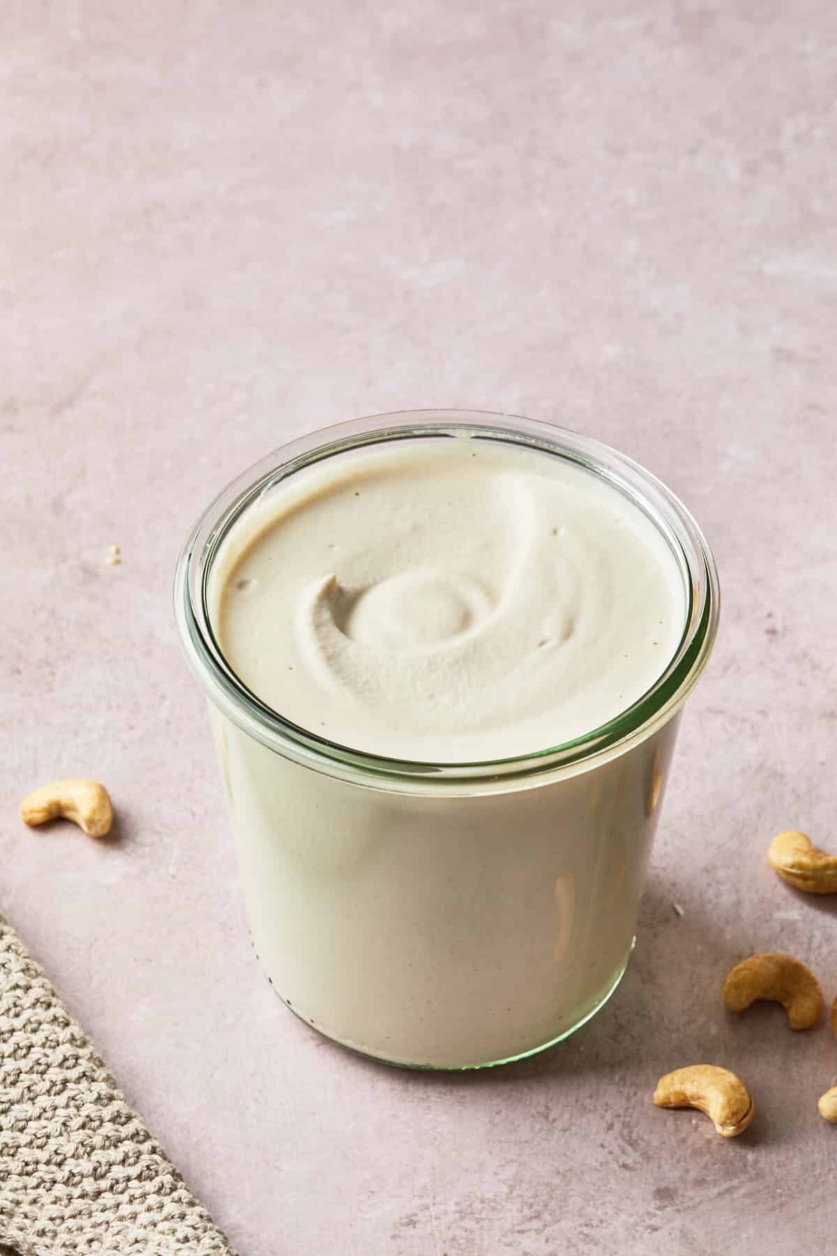 a jar of cashew cream with a few cashews on the surface next to the jar