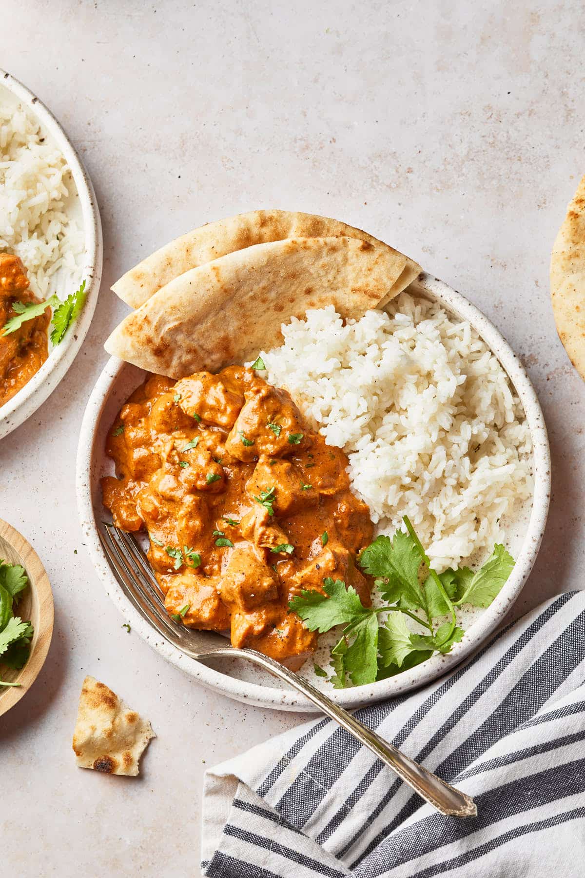 A plate of dairy free butter chicken garnished with fresh cilantro and served with basmati rice and garlic naan. 