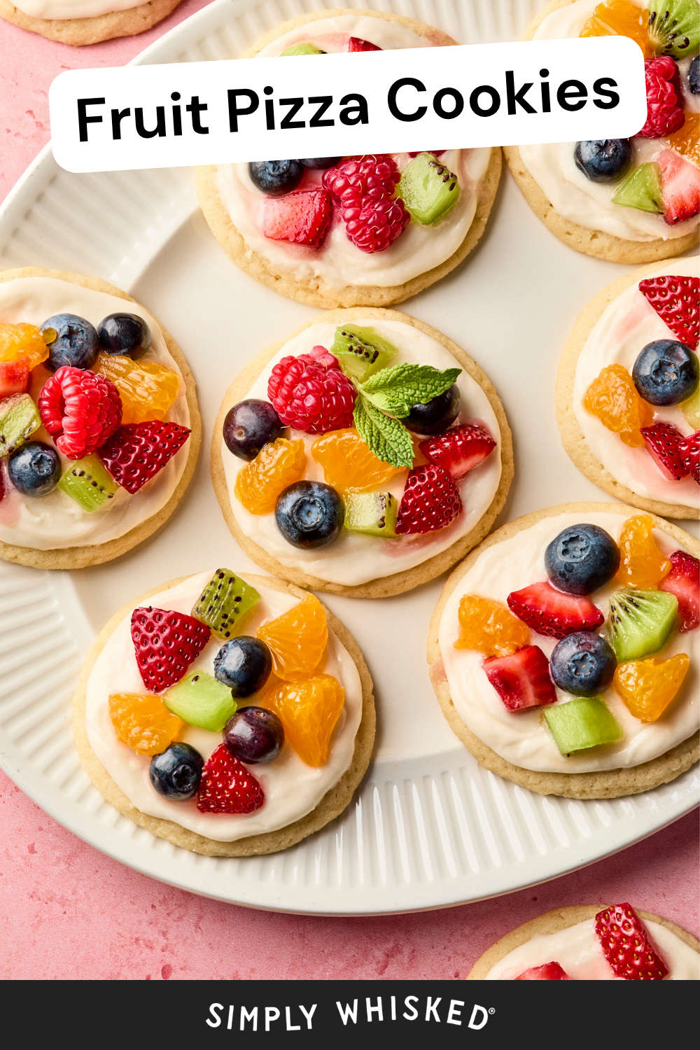A plate of fruit pizza cookies topped with white frosting and vibrant fresh fruit like strawberries, blueberries, kiwi, mandarin oranges, and raspberries. Text reads Fruit Pizza Cookies and Simply Whisked.
