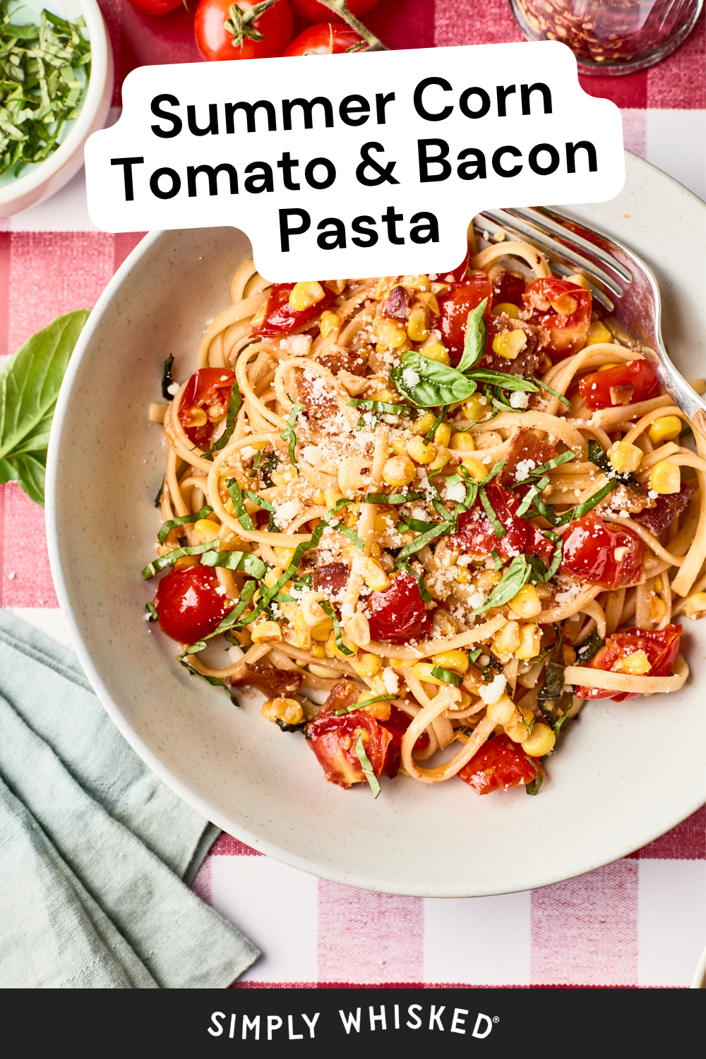 A bowl of bacon pasta topped with corn, tomatoes, basil, and grated cheese sits on a red and white checkered tablecloth. A fork rests in the bowl, surrounded by fresh ingredients. Text reads: Summer Corn Tomato & Bacon Pasta.