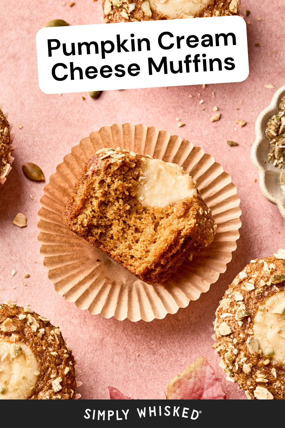 A pumpkin cream cheese muffin with a creamy center sits on a pink surface surrounded by more pumpkin cream cheese muffins. Text reads Pumpkin Cream Cheese Muffins and Simply Whisked at the bottom.