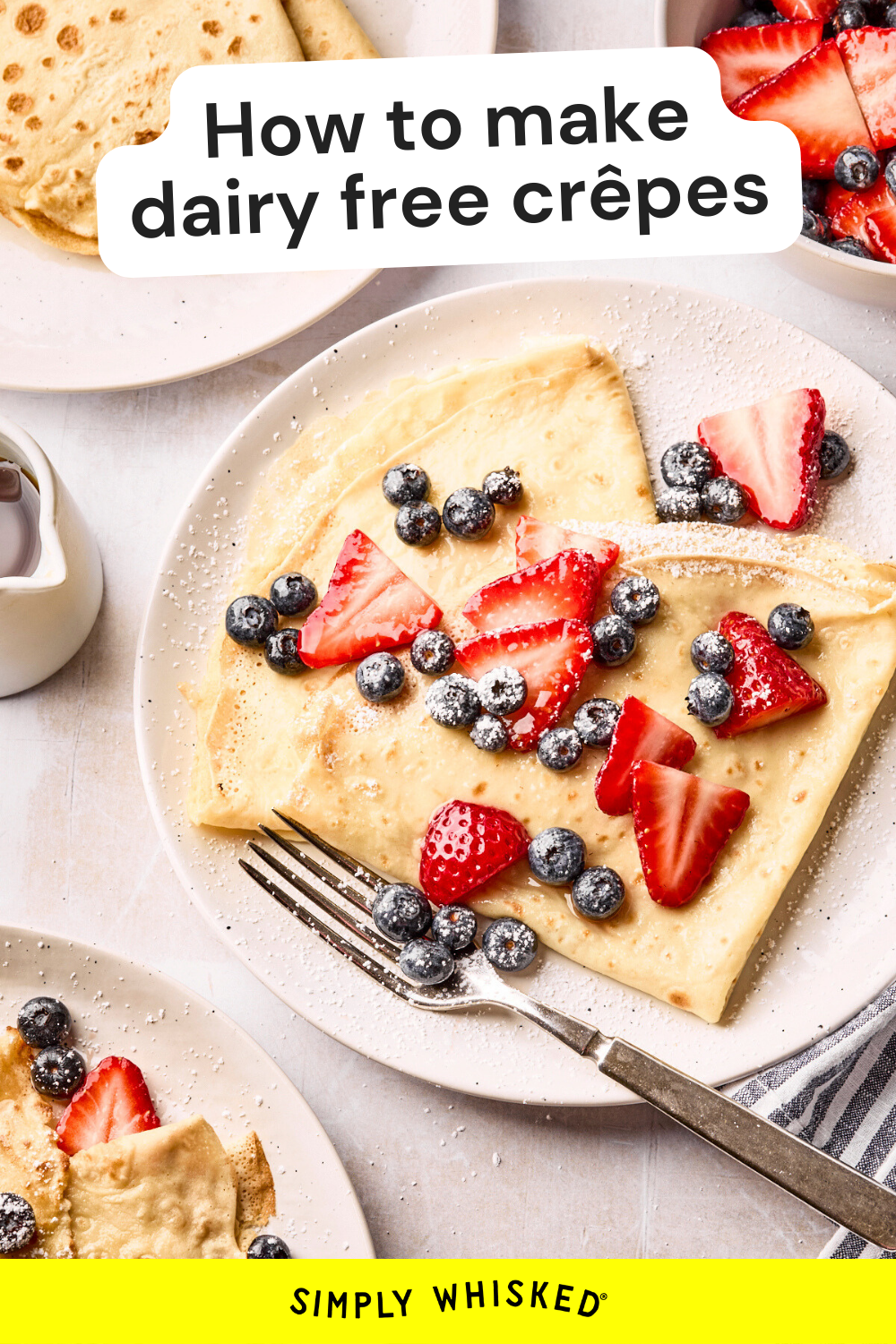A plate of dairy free crepes topped with sliced strawberries and blueberries, dusted with powdered sugar. A fork rests on the plate, and a small pitcher of syrup sits nearby. Text on image: How to make dairy free crêpes.