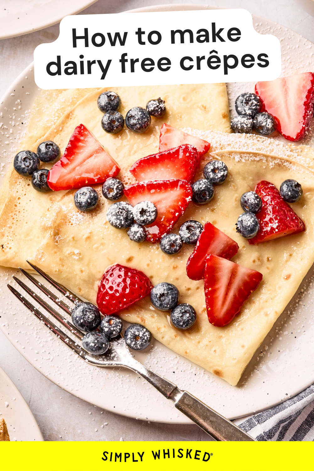 A plate of dairy free crepes topped with fresh strawberries, blueberries, and powdered sugar. A fork rests on the plate, and text reads, How to make dairy free crepes. The Simply Whisked logo appears at the bottom.