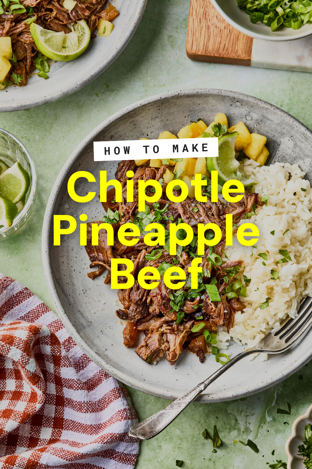 A plate of pineapple beef—shredded chipotle beef with juicy pineapple chunks, white rice, and chopped green herbs—sits by a fork. Nearby are bowls with lime wedges and green onions on a green surface with a red-checked napkin.