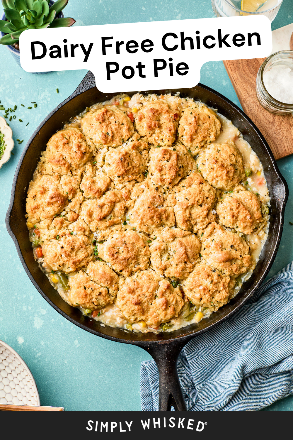 A skillet filled with easy chicken pot pie with biscuits, topped with golden, dairy-free biscuit pieces, is shown on a blue surface with a napkin and plates nearby. Text on the image reads Dairy Free Chicken Pot Pie.