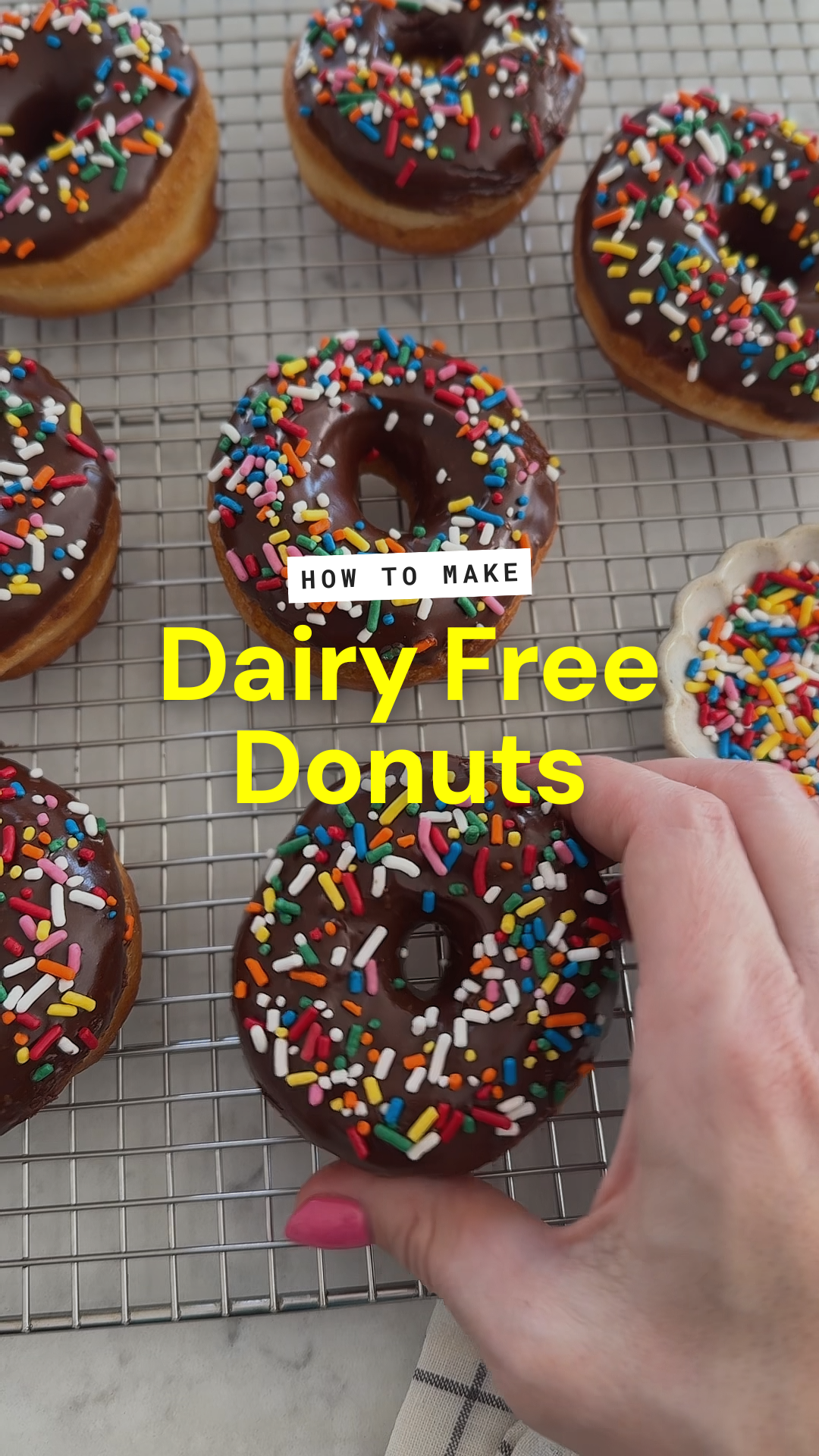 A hand holds a chocolate-glazed, sprinkle-topped dairy free donut over a rack of similar treats; text reads How to make Dairy Free Donuts.
