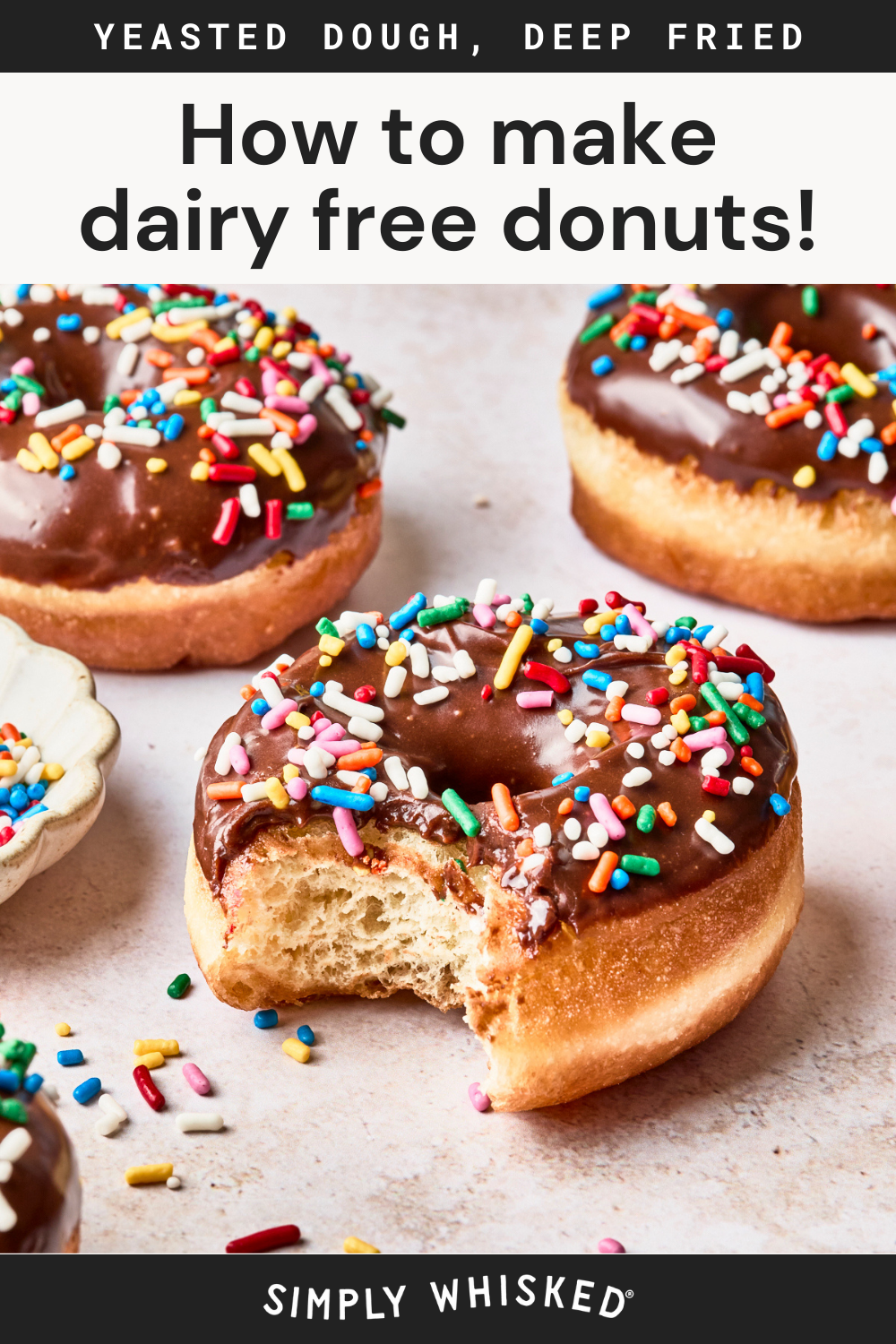 Chocolate glazed dairy free donuts with colorful sprinkles are arranged on a light surface, one with a bite taken out. Text above reads How to make dairy free donuts! and Yeasted dough, deep fried.