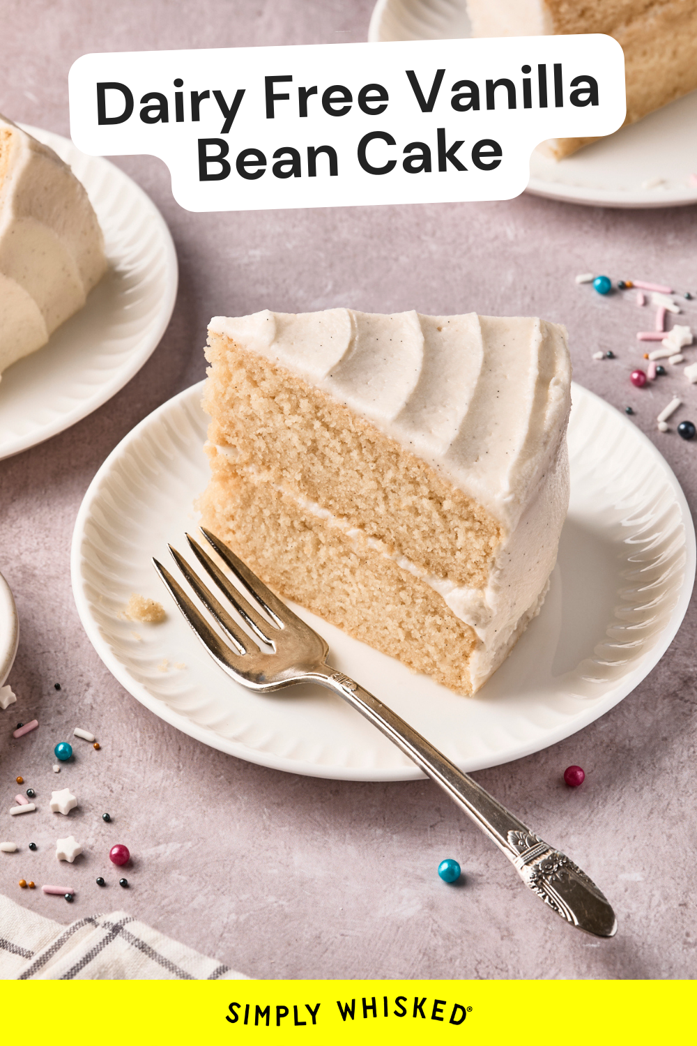 A slice of frosted dairy free vanilla cake sits on a white plate with a fork. Nearby, more slices and colorful sprinkles decorate the light surface. Text reads Dairy Free Vanilla Bean Cake.