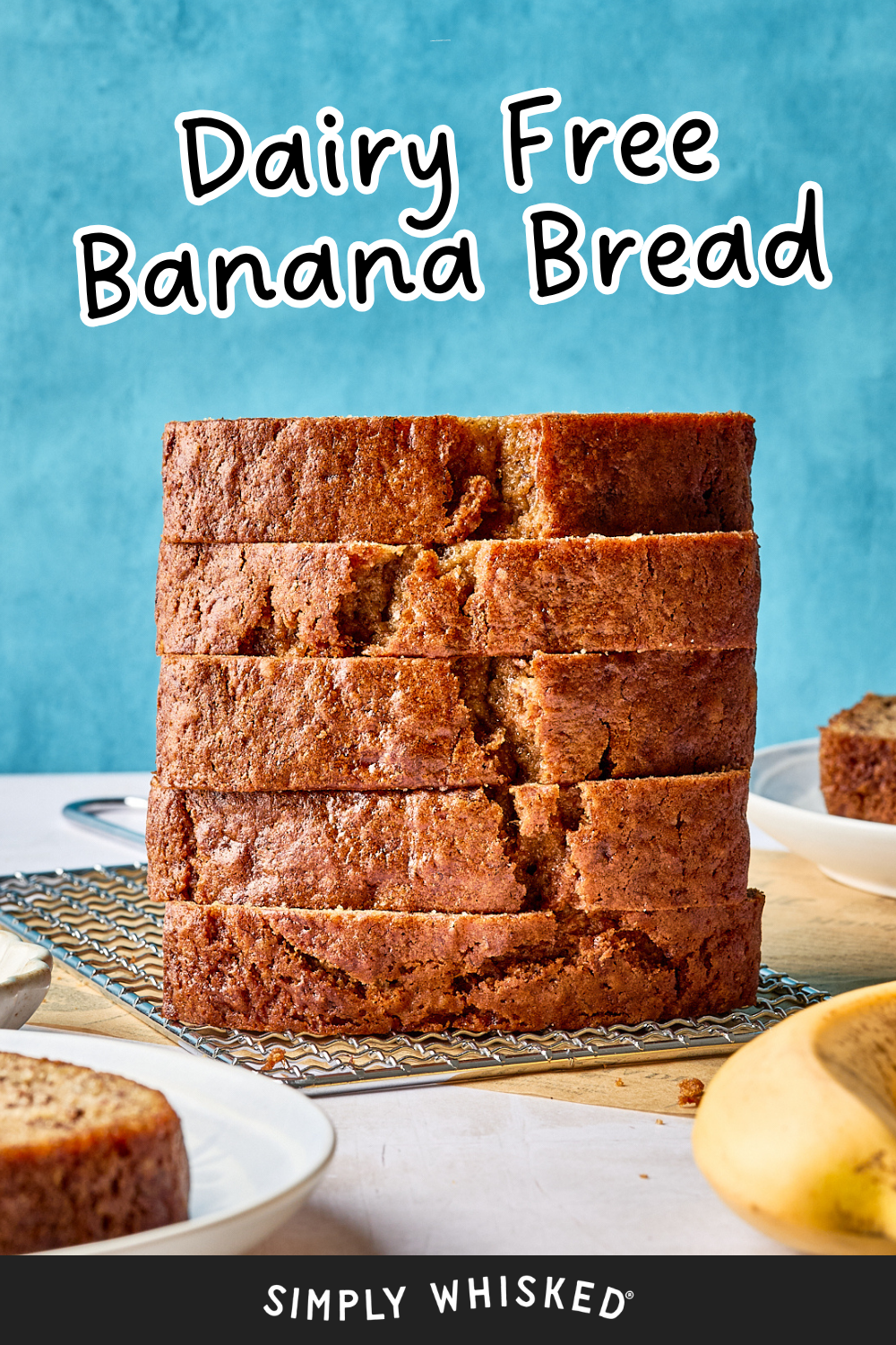 A stack of thick, golden-brown banana bread slices sits on a cooling rack, with text above reading Dairy Free Banana Bread. A banana and a plate with more banana bread are in the background.
