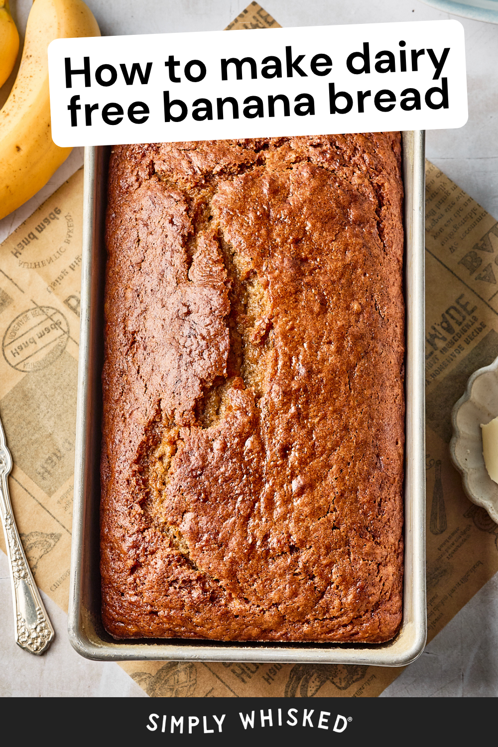 A loaf of golden-brown banana bread in a metal pan sits on a parchment-lined surface with a spoon, butter, and banana nearby. Text on the image reads, How to make dairy free banana bread.