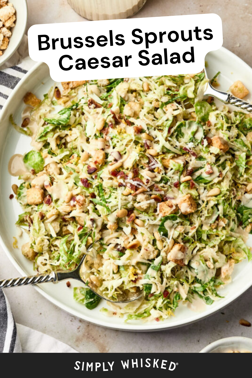 A large plate of Brussels sprouts Caesar salad featuring shredded sprouts, crunchy croutons, seeds, and a creamy Caesar dressing, served with two forks. Text on image: Brussels Sprouts Caesar Salad. Branding: Simply Whisked.