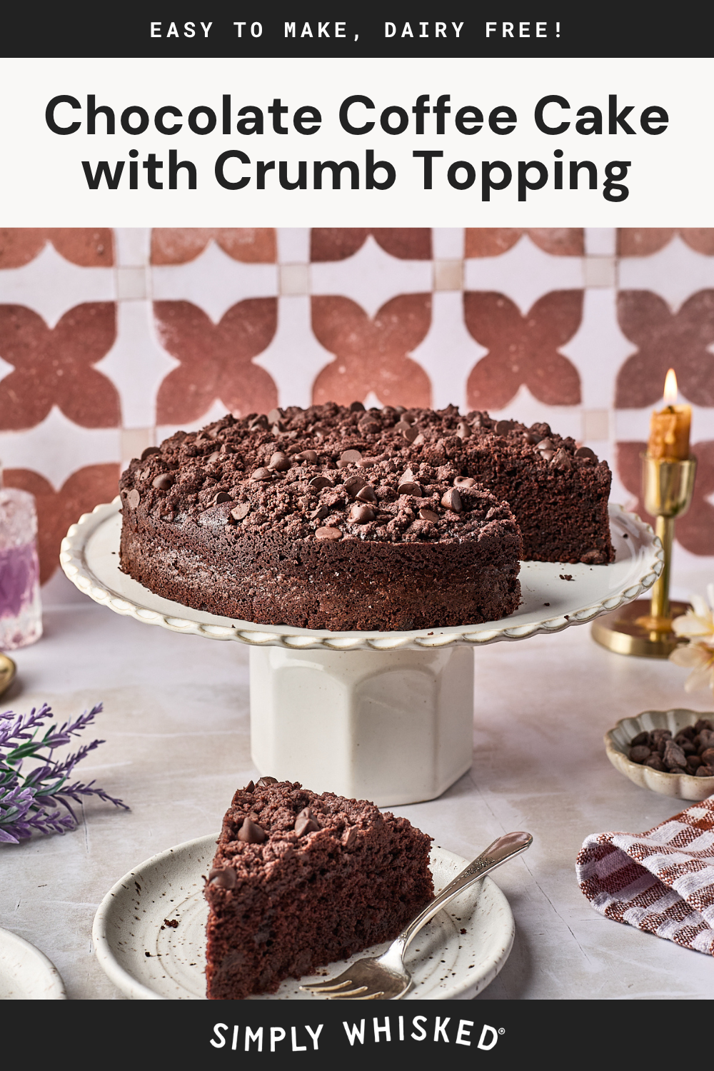 A chocolate coffee cake with crumb topping sits on a cake stand. A slice is on a plate with a fork. The background features a patterned wall, a candle, and a lavender sprig. Text states its dairy free.