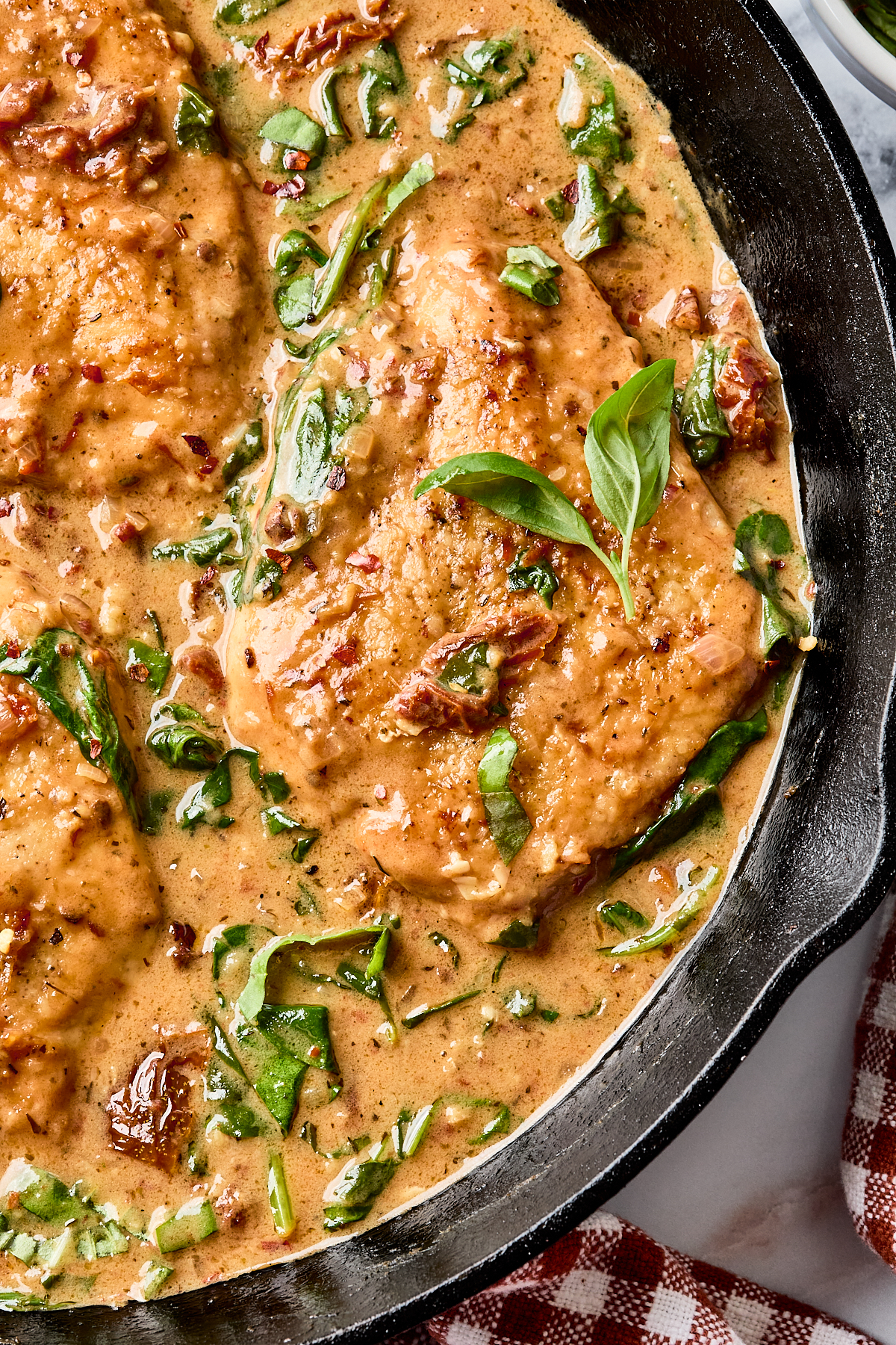 Chicken breasts in a creamy sauce with spinach and sun-dried tomatoes, garnished with fresh basil, cooked in a black skillet.