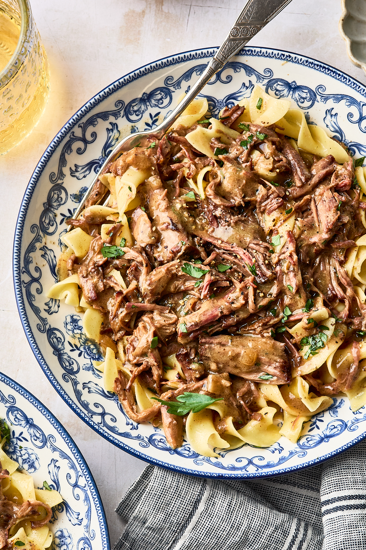 Beef stroganoff with shredded beef and egg noodles in a blue and white patterned bowl, with a silver spoon resting on top.