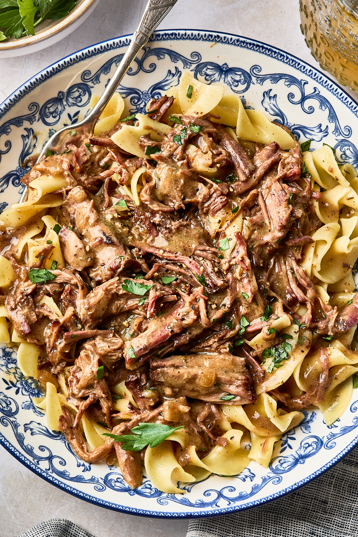 Shredded beef in a savory sauce served over buttered egg noodles in a blue and white patterned bowl.